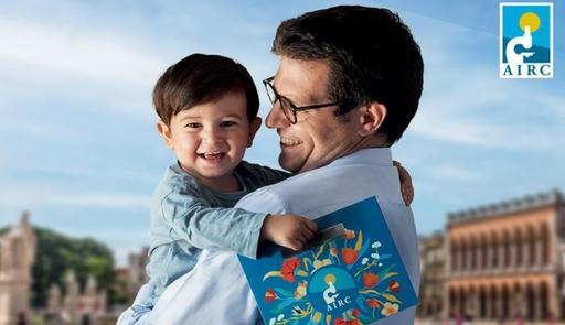 un uomo che tiene in braccio un bambino sorridente che tiene in mano la scatola di cioccolatini