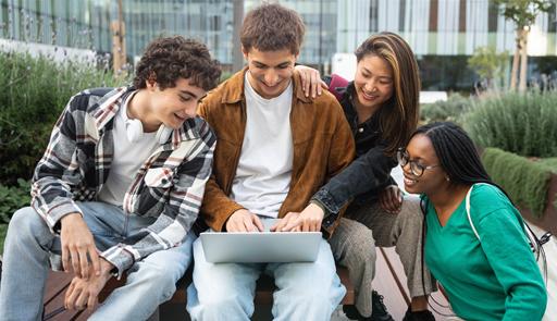 Studenti e studentesse Quattro studenti sorridenti, due ragazzi e due ragazze, sono seduti in uno all'aperto, guardano un pc portatile