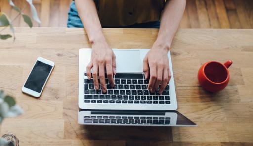 Mani femminili che lavorano ad un pc portatile poggiato su un tavolo di legno