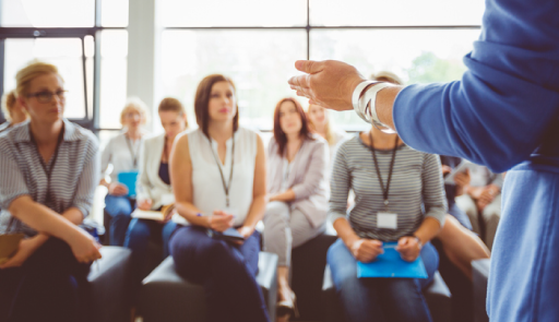Immagine di una docente, della quale si intravvedono solo le mani, in aula di lezione di fronte ad una platea di altre donne