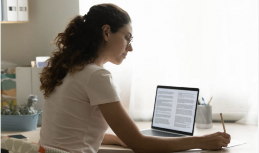Ragazza alla scrivania scrive su carta guardando un testo al pc