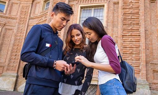 tre studenti stranieri nei pressi di palazzo Carignano guardano uno smartphone