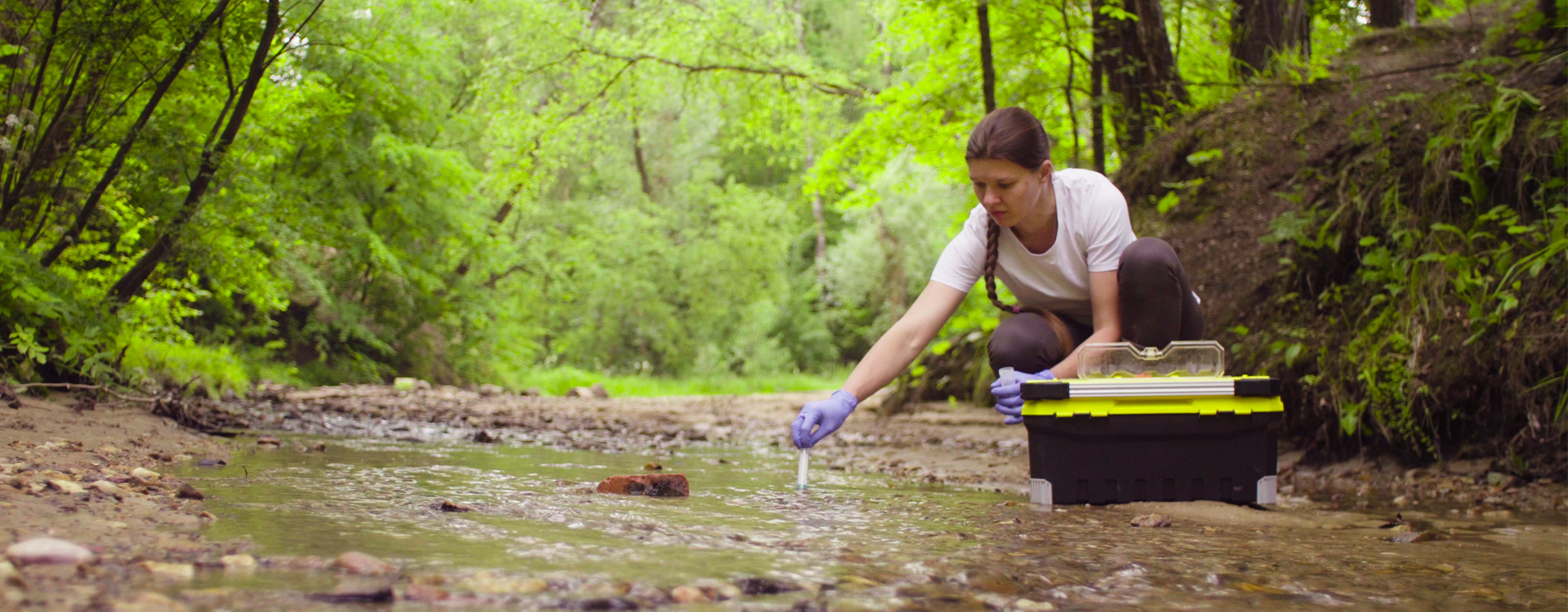 Una ragazza usa uno strumento per prelevare un campione d'acqua da un piccolo corso d'acqua