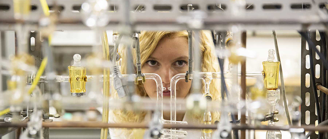 Ricercatrice in laboratorio dietro a una serie di ampolle trasparenti